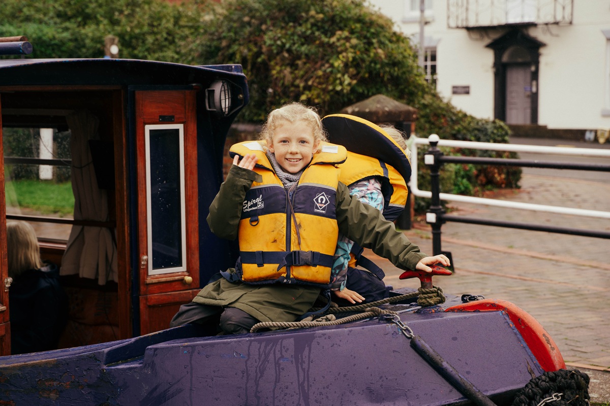 A child waving and wearing a life jacket