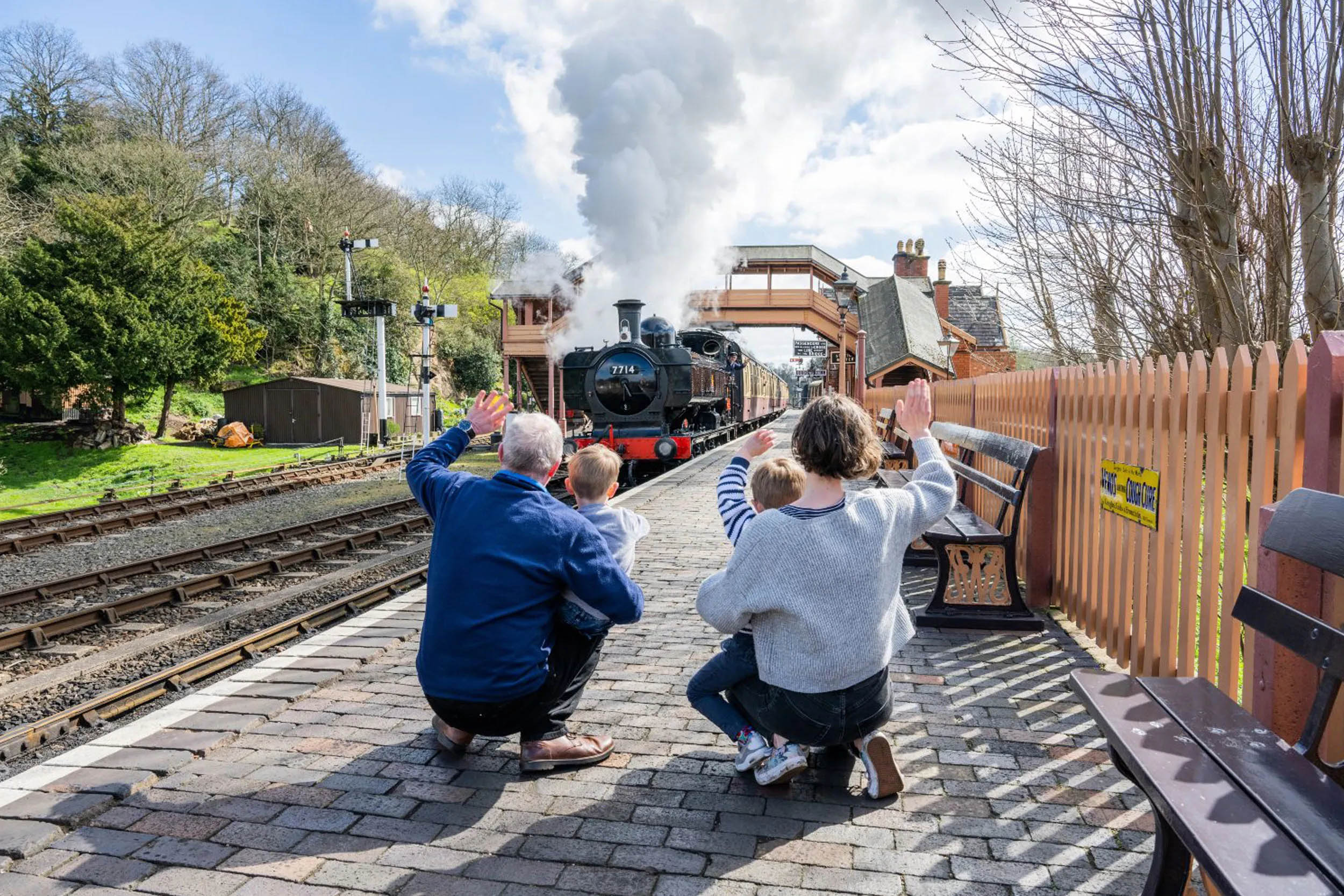 Two adults and two children waving at a steam train